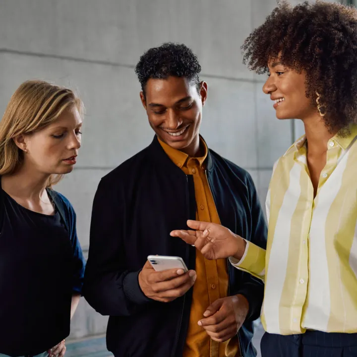 Group of two women and a man, smiling and looking on a phone.